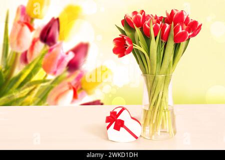 Modèle de carte de vœux. Bouquet décoratif de tulipes rouges et une boîte cadeau en forme de coeur sur table sur fond flou. Printemps, valentine, mothe Banque D'Images