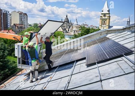 Ouvriers construisant un système de panneau solaire sur le toit en métal avec l'aide d'un ascenseur de grue en milieu urbain. Hommes installateurs transportant le module solaire photovoltaïque à l'extérieur. Concept de génération d'énergie renouvelable. Banque D'Images