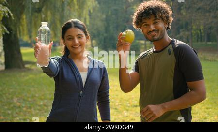 Homme indien et femme se relaxant après le sport ensemble dans le parc à l'extérieur Arabian Fitness couple amis dans le sport de ville heureux gens montrant tenant la pomme Banque D'Images