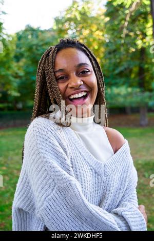 Heureuse jeune femme noire, debout dehors dans un parc public regardant la caméra souriant. Banque D'Images