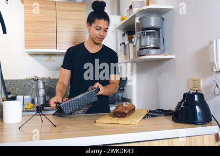 Jeune homme latino-vénézuélien, debout dans le bureau de sa maison servant gâteau fraîchement cuit sur planche à découper, concept de nourriture, espace de copie. Banque D'Images