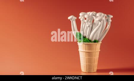 Gros plan d'un bouquet de champignons shimeji avec de la mousse verte dans un cône de crème glacée, sur fond orange, superaliment, un type de délicieux champignons à huîtres, HE Banque D'Images