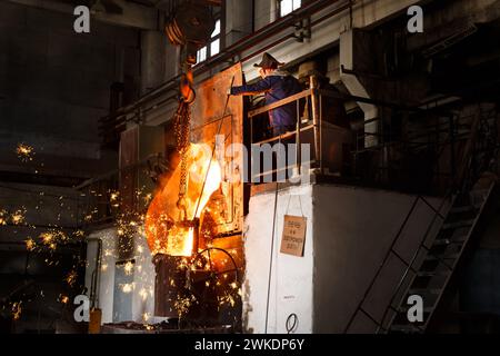 Travailleur gère la coulée de métal fondu dans l'environnement industriel, production d'acier four à haute température, étincelles volant, expert en métallurgie supervise Banque D'Images