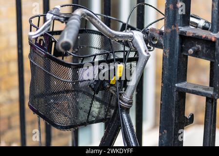 Un vieux vélo avec un panier avant enchaîné à une rampe de clôture. Banque D'Images