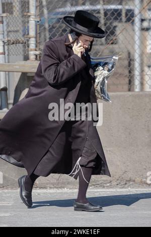 Un homme juif orthodoxe parle sur son téléphone à clapet alors qu'il rentre chez lui après les services de prière du matin. Par une journée venteuse d'hiver à Brooklyn, 2024 Banque D'Images