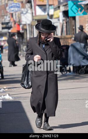 Un homme juif hassidique marche sur Lee Ave. tout en parlant sur son téléphone à clapet. À Williamsburtg, Brooklyn, New York. Banque D'Images