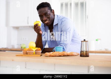 Homme d'Afrique mange des pommes dans la cuisine pendant le petit déjeuner Banque D'Images