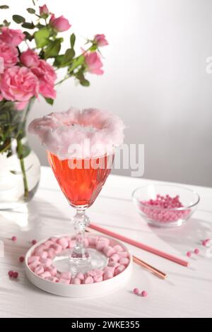 Cocktail de barbe à papa en verre, guimauves, vase avec des roses roses et des pailles roses sur une table en bois blanc sur fond gris Banque D'Images