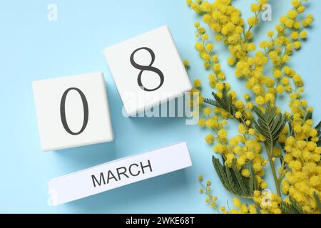 8 mars - Journée internationale de la femme. Conception de carte de voeux avec de belles fleurs de mimosa jaune et calendrier en bois sur fond bleu clair, fla Banque D'Images