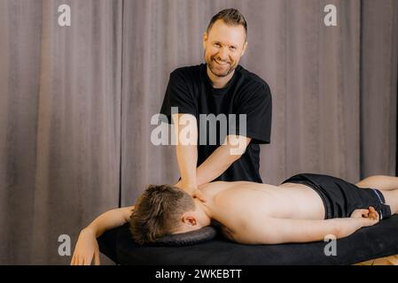 Soulager la tension musculaire du dos. Masseur professionnel massant le dos du jeune homme en utilisant tapement ou hachage, tapotement ou technique de piratage pendant Banque D'Images