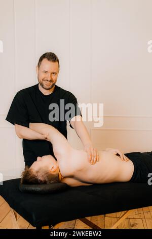 Soulager la tension musculaire du dos. Masseur professionnel massant le dos du jeune homme en utilisant tapement ou hachage, tapotement ou technique de piratage pendant Banque D'Images