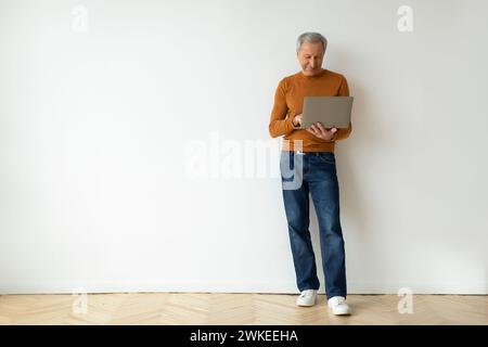 Grand-père avec ordinateur portable dans ses mains sur fond de mur blanc Banque D'Images