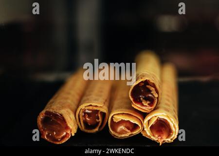 Petits pains de gaufrettes sucrés avec du lait condensé au chocolat sur fond sombre Banque D'Images