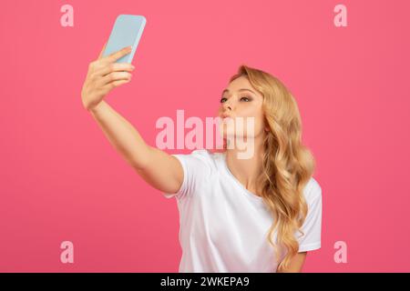 Ludique Blonde Lady faire Selfie sur téléphone pouting lèvres, Studio Banque D'Images