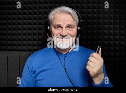 Traitement de la perte auditive. Homme senior positif portant un casque d'audiométrie pendant un test auditif et un audiogramme dans une salle audio spéciale Banque D'Images