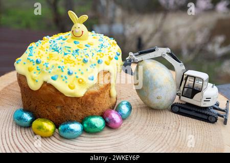 Modèle d'une pelle de jouet à côté d'un grand œuf de Pâques, d'un gâteau de vacances et de bonbons au chocolat multicolores Banque D'Images