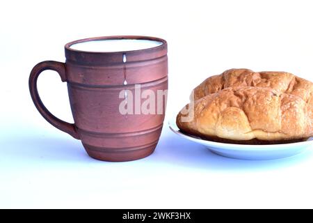 L'image montre un verre en argile brune avec du lait versé dedans et des gouttes de lait sur les parois du récipient, et à côté de lui il y a deux bu Banque D'Images