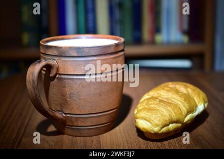 La photo montre une tasse en argile brune avec du lait versé dedans et du kraussan sur une assiette. Banque D'Images