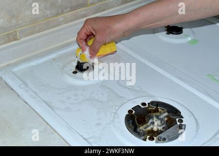 La femme lave la surface supérieure de la cuisinière à gaz autour du petit brûleur avec une éponge et des détergents. Banque D'Images