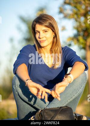 Femme détendue regardant la caméra tout en étant assis à l'extérieur dans un parc pendant le coucher du soleil. Banque D'Images