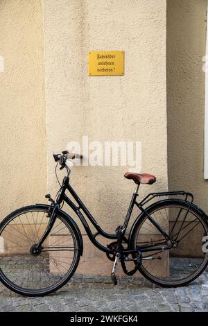 Un vélo appuyé contre un mur de maison jaune et verrouillé sous un panneau jaune avec l'inscription allemande en vieilles lettres : Fahhrad anlehnen verboten Banque D'Images
