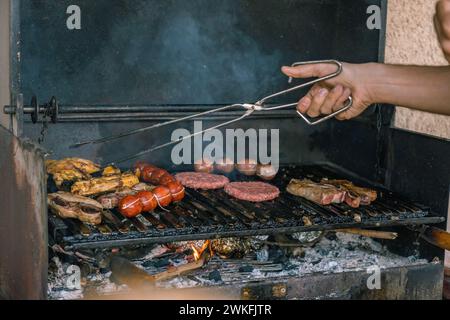 Gros plan des mains d'un homme avec des pinces tournant la viande sur le gril pendant un barbecue Banque D'Images