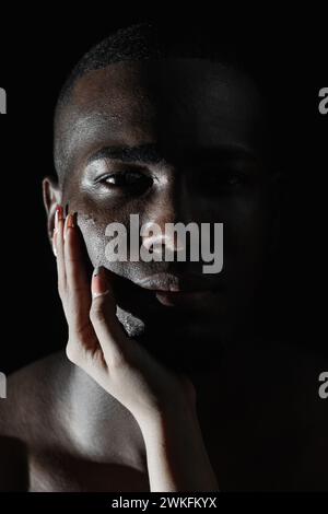 Gros plan du visage d'un homme afro-américain avec la main d'une femme caucasienne sur la joue. lumière à 90 degrés. Banque D'Images