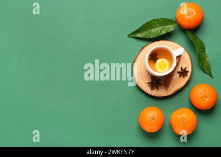 Planche en bois avec tasse de thé, mandarines savoureuses et épices sur fond vert Banque D'Images