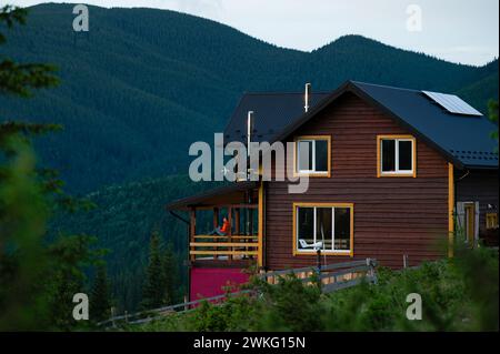 Une grande maison en bois pour les touristes dans les montagnes, une jeune fille se dresse sur la terrasse sur fond des Carpates, une maison pour Banque D'Images