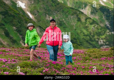 Une mère avec son fils et sa fille marchent parmi les buissons de rhododendrons sur fond de la majesté des Carpates, somme active Banque D'Images