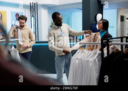 Femme asiatique souriante tenant la veste et demandant conseil de boutique pour la mode tout en magasinant pour la tenue formelle. Client et employé du magasin de vêtements discutant des vêtements pour femmes Banque D'Images