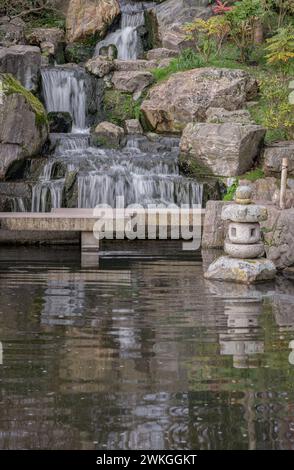 Lanterne décorative japonaise en pierre devant avec des érables orange et un pont. Cascade longue exposition cascade lisse soyeuse sur les falaises rocheuses dans Banque D'Images