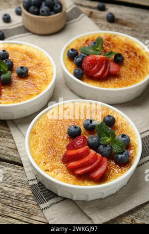 Délicieuse crème brûlée avec des baies et de la menthe dans des bols sur une table en bois Banque D'Images