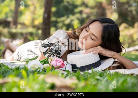 Une femme asiatique insouciante et attrayante s'endort ou fait une sieste sur un tapis de pique-nique dans un parc ou un jardin verdoyant. Banque D'Images