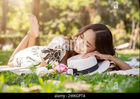 Une femme asiatique insouciante et attrayante s'endort ou fait une sieste sur un tapis de pique-nique dans un parc ou un jardin verdoyant. Banque D'Images