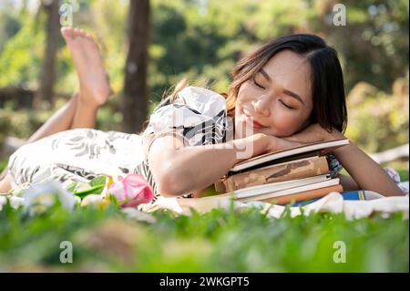 Une femme asiatique insouciante et attrayante s'endort ou fait une sieste sur un tapis de pique-nique dans un parc ou un jardin verdoyant. Banque D'Images