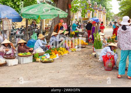 Ville de Hue, Vietnam 21 mars 2015 : femmes ornées de chapeaux traditionnels vendant des fleurs colorées au marché de rue extérieur animé à l'ombre de parapluies, wi Banque D'Images