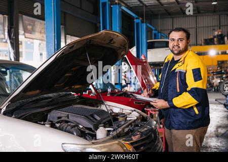 Ouvrier de mécanicien automatique de garage de portrait travaillant en vérifiant le moteur de voiture dans le centre de service de voiture, travail masculin professionnel indien Banque D'Images