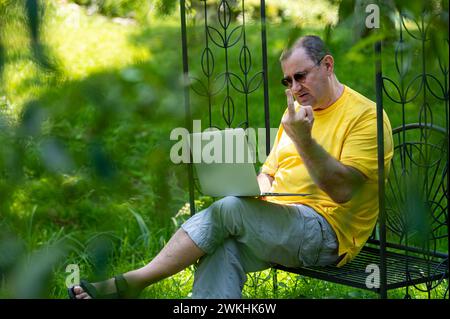 homme mûr avec ordinateur portable travaillant à l'extérieur dans le jardin et montre le mouvement du doigt central dans le moniteur Banque D'Images