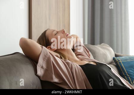 Vue latérale de la jeune jolie femme se relaxant sur le canapé confortable. Banque D'Images