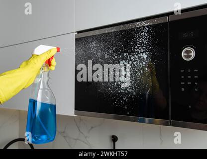 Spray anti-graisse dans la main d'une fille qui nettoie la cuisine. Nettoyer le four à micro-ondes de la graisse et de la saleté. Agent antistatique moderne. Banque D'Images