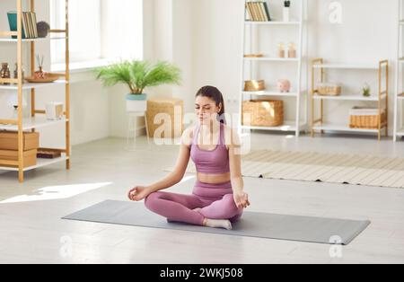 Jeune femme sportive souriante faisant de l'exercice de yoga à la maison assise dans la pose de lotus. Banque D'Images
