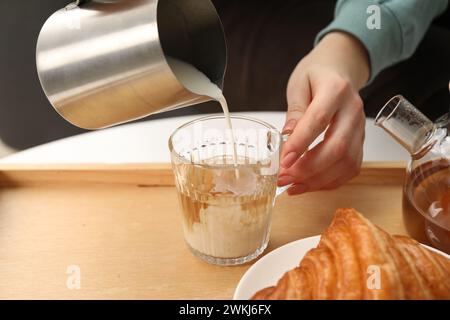 Femme versant du lait dans la tasse avec du thé aromatique à la table à l'intérieur, gros plan Banque D'Images