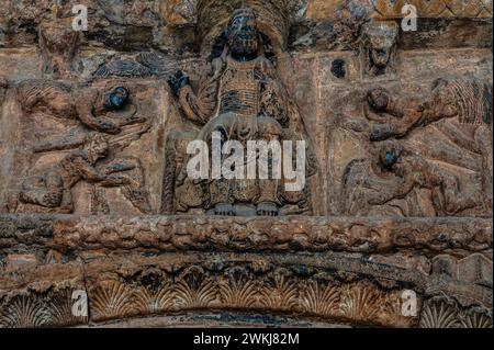 Christ en Majesté, dans de somptueuses robes et soutenu par des anges. Sculpté en relief au sommet de l'entrée de la basilique du monastère de Santa Maria de Ripoll dans la province de Gérone, Catalogne, Espagne. L'entrée a été sculptée au milieu des années 1100 dans un style roman lombard. Banque D'Images