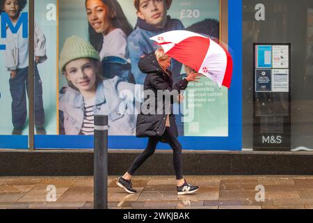 Femme avec parapluie de golf rouge et blanc à Preston, Lancashire. Météo britannique. 21 février 2024. Vents forts et fortes pluies pour les acheteurs dans le centre-ville. Crédit ; MediaWorldImages/AlamyLiveNews Banque D'Images