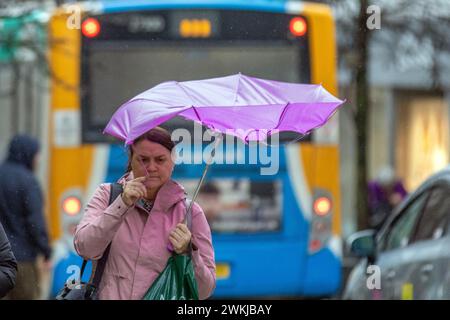 Femme avec parapluie de golf rouge et blanc à Preston, Lancashire. Météo britannique. 21 février 2024. Vents forts et fortes pluies pour les acheteurs dans le centre-ville. Crédit ; MediaWorldImages/AlamyLiveNews Banque D'Images