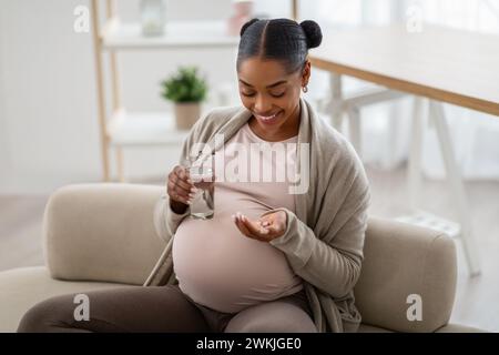 Souriante jeune femme enceinte afro-américaine tenant une poignée de pilules Banque D'Images