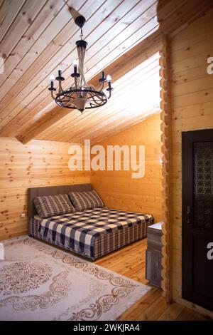 La chambre est décorée avec des lambris de bois chaleureux et un lit doux et accueillant. Un beau lustre fournit un éclairage doux. Banque D'Images