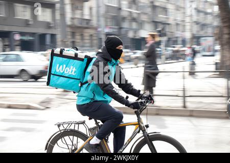 Belgrade, Serbie - 20 février 2024 : Wolt service de courrier avec un sac de livraison vélo dans la rue animée de la ville pleine de piétons, vue de profil Banque D'Images