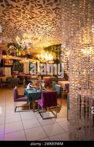 Un élégant intérieur de restaurant avec des chaises violettes, des nappes vertes, des lustres et des fleurs murales décoratives créant une atmosphère chaleureuse. Banque D'Images